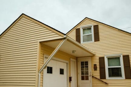 Close up of. a yellow wood-sided house with brown shutters and white windows and doors.