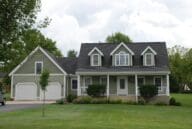 Sage green farmhouse-style residence with a grassy front lawn and an attached two-car garage.