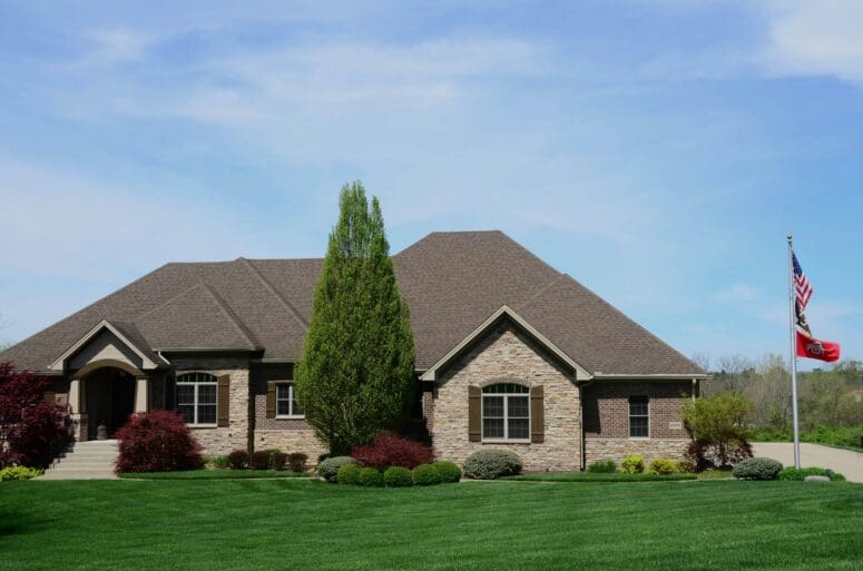 Large contemporary stone and brick house with wood shutters. The house has a grassy front lawn with a flag pole with an American flag and an Ohio State flag.