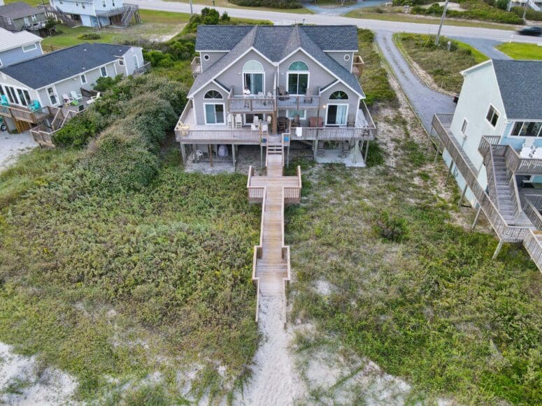Drone shot of a gray, multi-story beach house on Topsail Beach in North Carolina. There is a wooden boardwalk that extends from the house to the sandy beach.