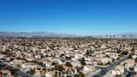 An aerial view of Las Vegas with snow-capped mountains and the Las Vegas Strip in the background. In the foreground are suburban single-family homes.