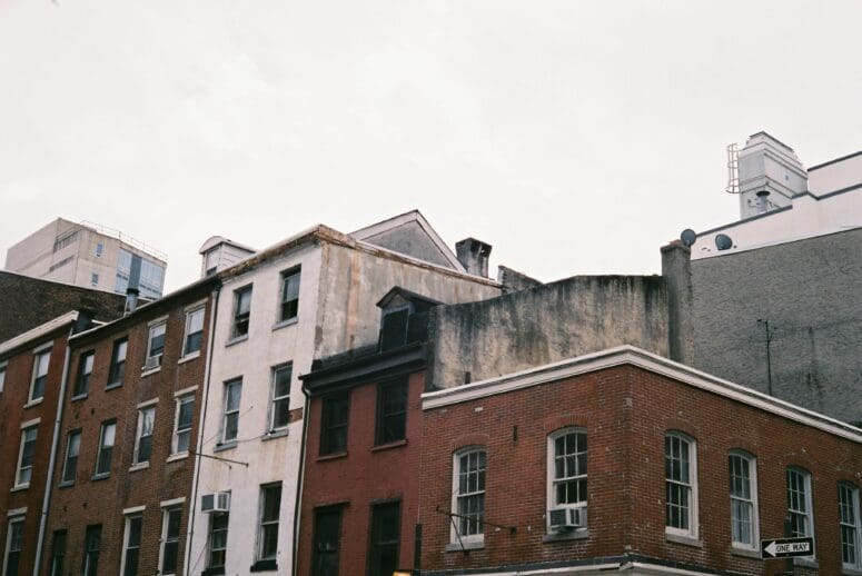 A row of brick and plaster residential buildings in South Philly. The sky is kind of gray and some of the windows have AC units sticking out of them.