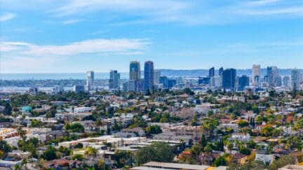 Drone shot of San Diego, showing the buildings downtown and the ocean and hillsides beyond.